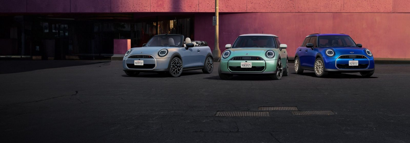 A MINI Cooper S Convertible, MINI Cooper S 2 Door, and MINI Cooper S 4 Door parked side by side in front of a salmon-colored concrete building.